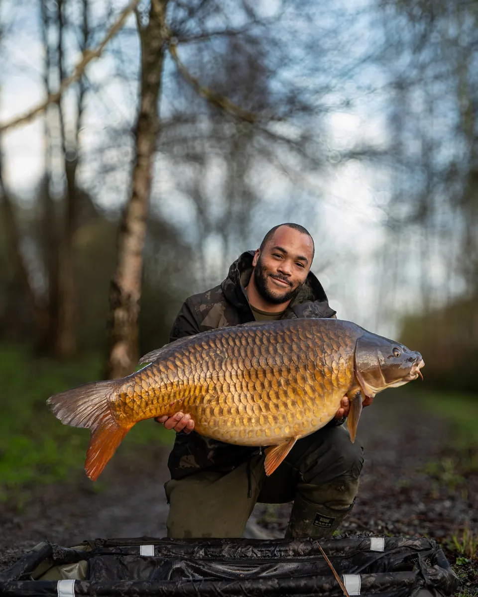 Jermaine holding a big golden common carp in autumn woodland