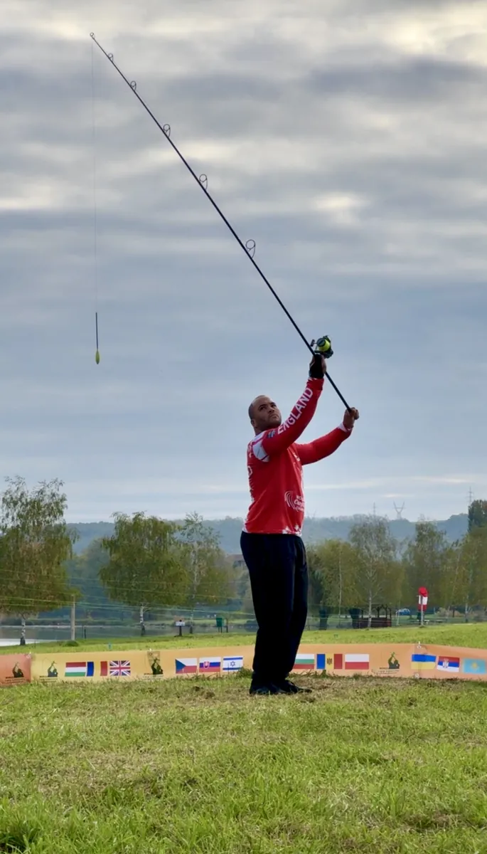 Jermaine casting in his England jersey at the World Carp Casting Championship venue, flags behind